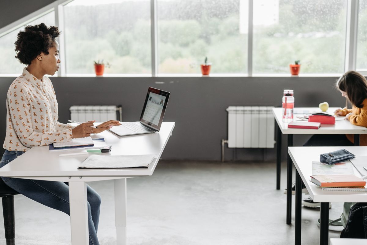 Docente al computer in un'aula luminosa, con studenti al lavoro